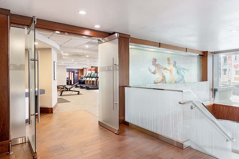 Modern fitness center entrance with glass doors, wooden framing, and gym equipment visible through windows