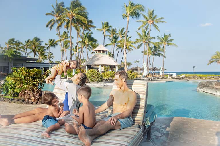Family relaxing poolside with tropical palm trees and ocean view