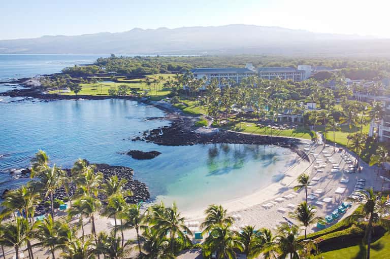 Aerial view of tropical beach resort with white sand, palm trees, and coastal mountains