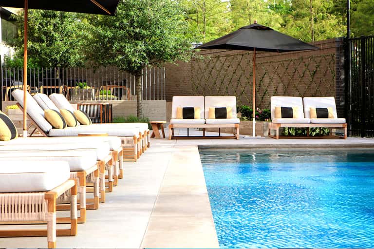 Luxury poolside lounge with white cushioned seating, black umbrella, and stone deck by pool