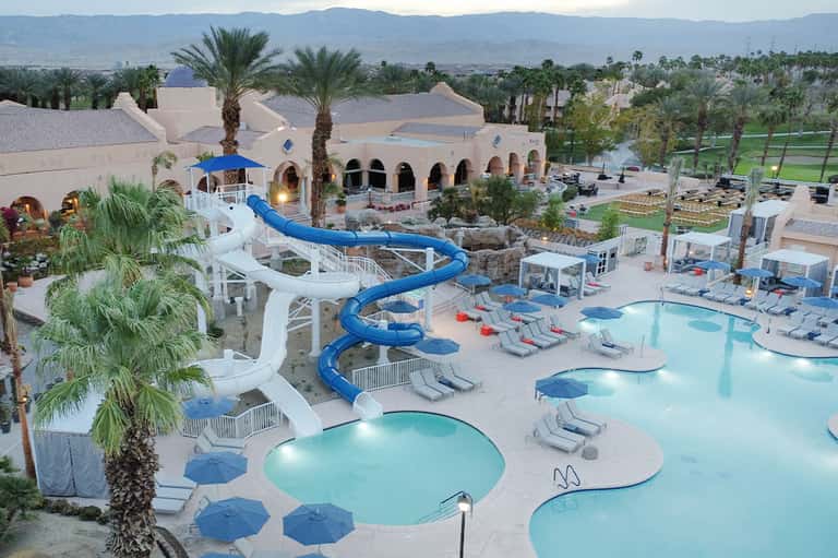 Aerial view of resort with white buildings, blue water slides, and palm trees