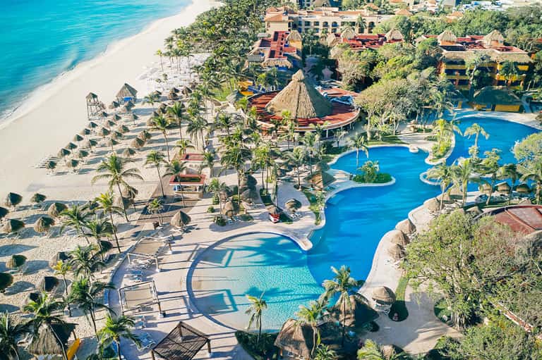 Aerial view of beachfront resort with curved pools, palm trees, and sandy beach