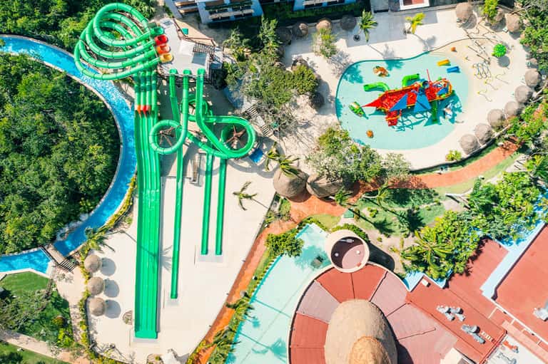 Aerial view of water park with green slides, multiple pools, and surrounding tropical landscaping