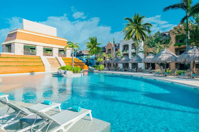 Resort main pool with large orange water slide feature, thatched umbrellas, and colorful buildings