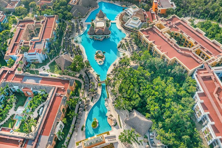 Aerial view of sprawling tropical resort with massive turquoise lagoon pool and red-roofed buildings