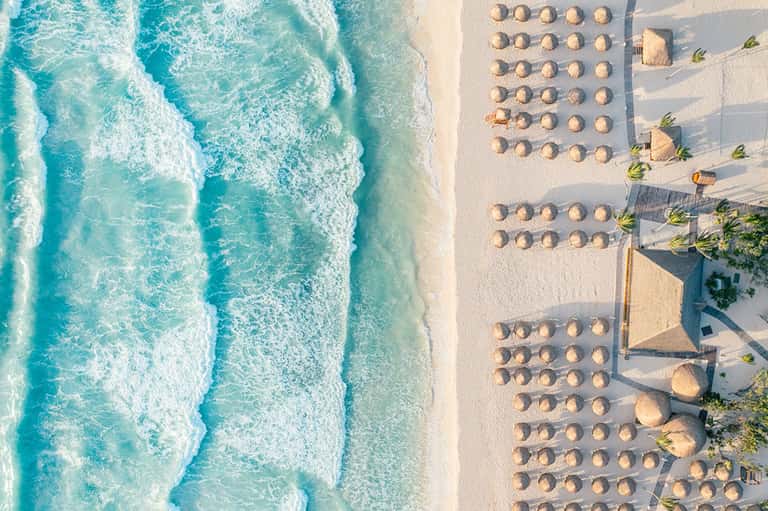 Overhead view of pristine beach with turquoise waves, rows of beach umbrellas and loungers