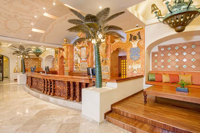 Luxurious hotel lobby with ornate wooden details, decorative palm tree, carved reception desk, and colorful artwork