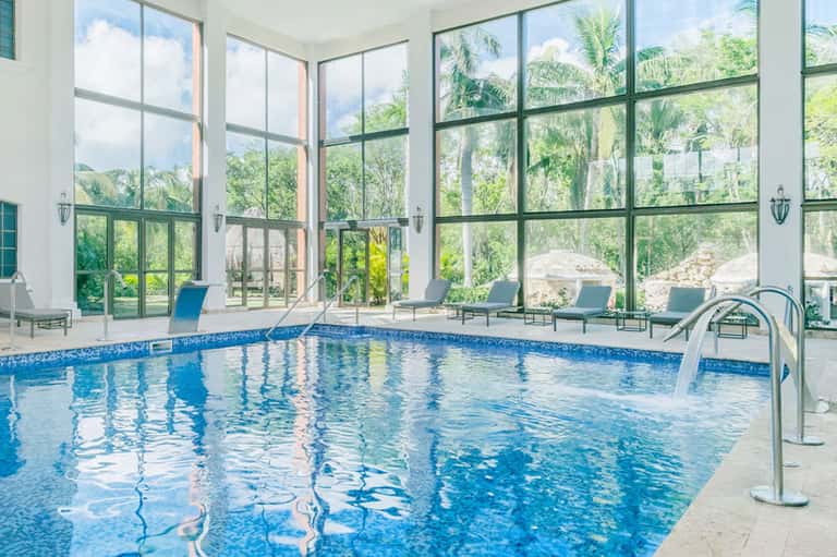 Indoor swimming pool with floor-to-ceiling windows, lounge chairs, and mountain views