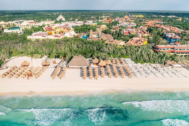 Aerial view of beachfront resort with rows of thatched umbrellas and loungers on white sand