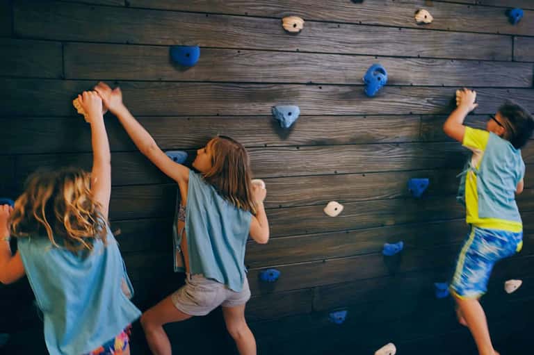 Children climbing indoor rock wall with colorful holds in recreation room
