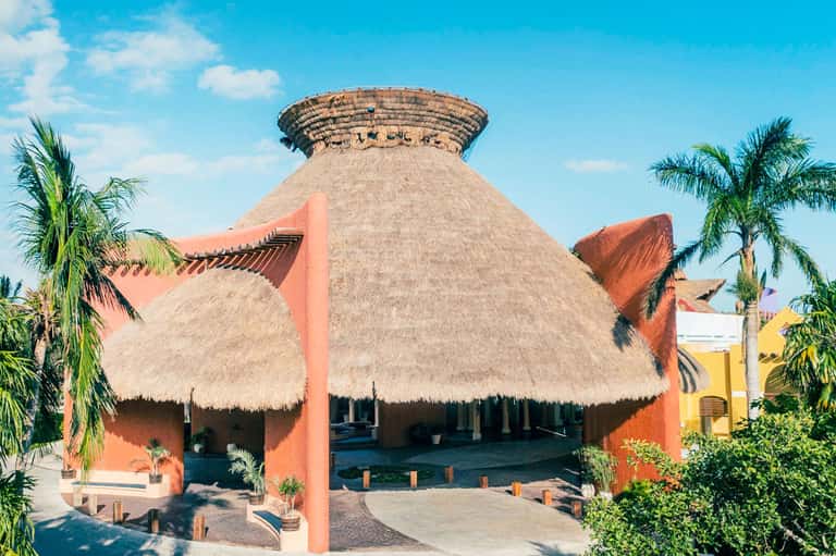 Striking orange and tan thatched-roof architectural structure with palm trees