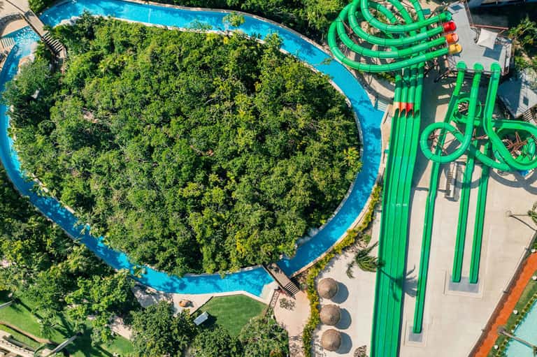 Aerial view of resort with blue lazy river, lush green vegetation, and bright green water slide structure