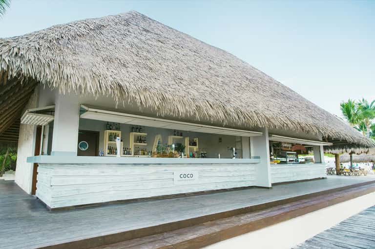 Beachfront tiki bar with thatched roof and white wooden counter on sandy shore