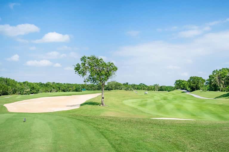 Manicured golf course with sand bunkers, trees, and fairways under clear blue sky