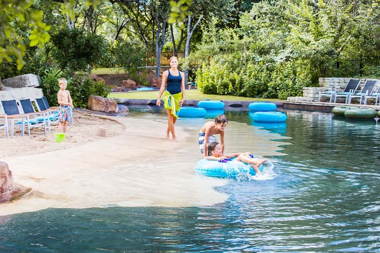 Family enjoying natural spring water with float tubes, sandy beach, trees, and resort facilities
