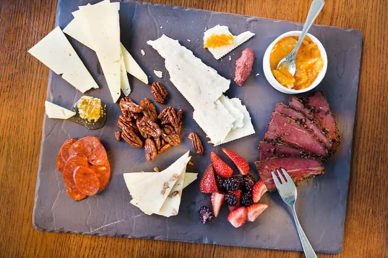 Charcuterie board with cheeses, cured meats, nuts, berries, and jam served on dark slate with fork