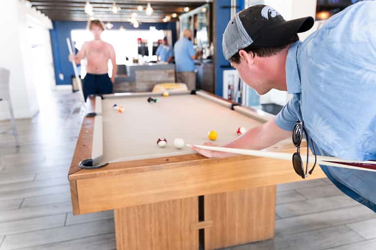 Man playing pool billiards in a casual recreation area with exposed brick and bright lighting.