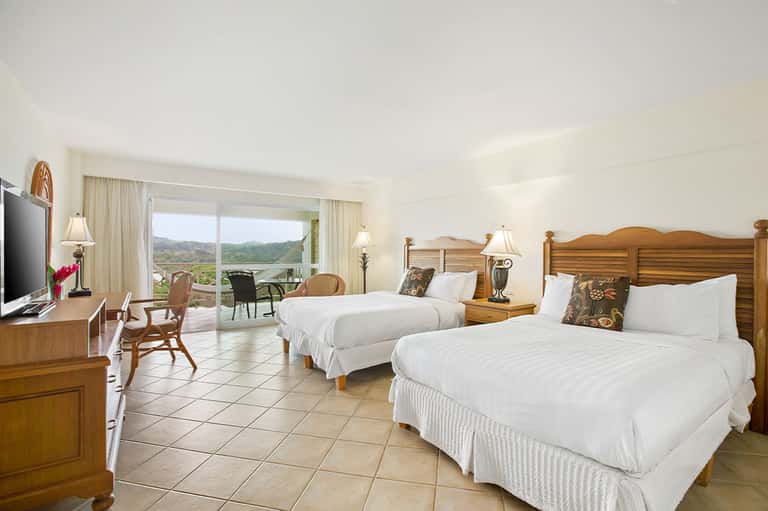 Spacious hotel room with two queen beds, wooden furniture, and balcony overlooking valley