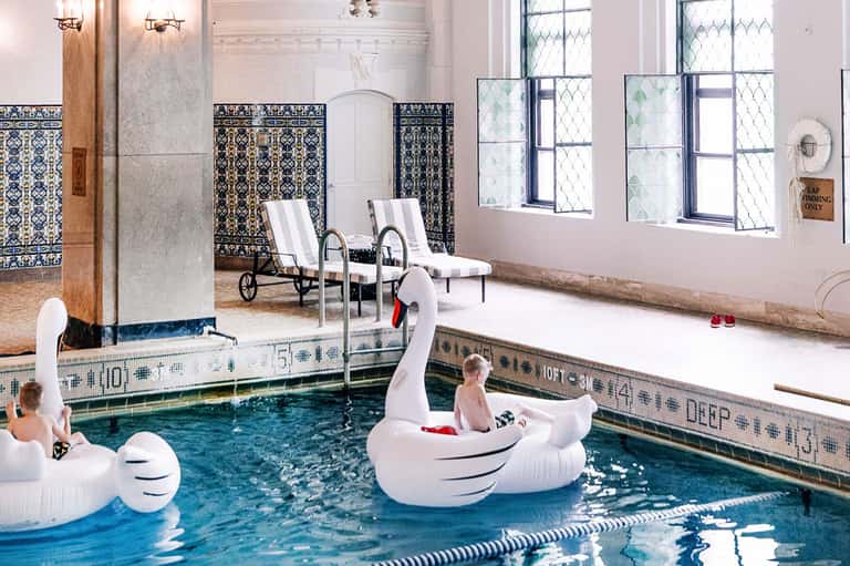 Indoor pool facility with decorative tile work, loungers, and children playing on floats