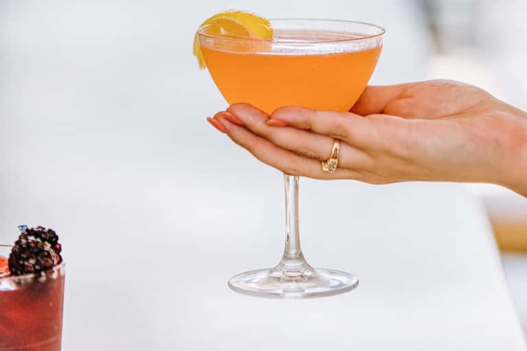Woman holding vibrant orange cocktail with orange slice garnish and gold ring