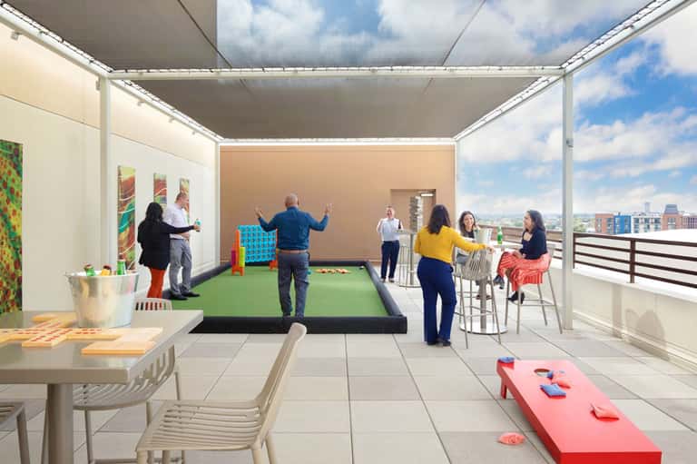 Rooftop lounge area with cornhole game, dining tables, and panoramic city views
