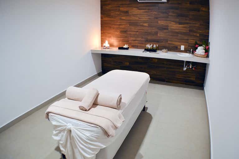 Spa massage treatment room with white bed, dark wood accent wall, and ambient candlelit counter