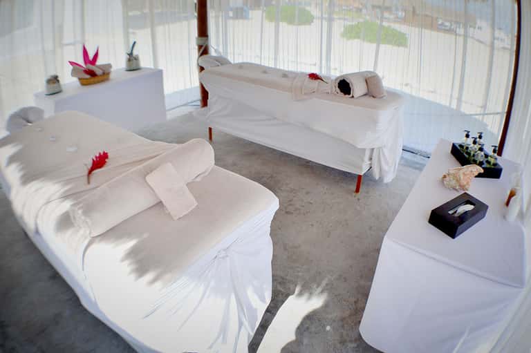 Spa treatment room with white draped massage beds and decorative elements on shelves
