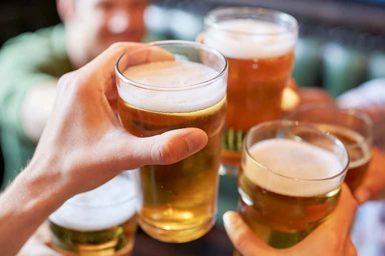 Group of people holding glasses of beer outdoors, toasting together