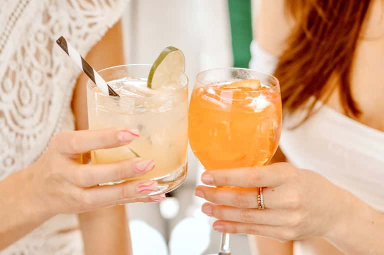 Two women holding tropical cocktails with decorative straws and citrus garnishes at a resort