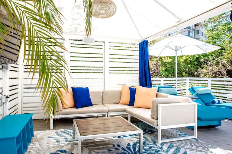 Modern rooftop lounge with beige sectional sofa, blue accents, and palm leaf decor