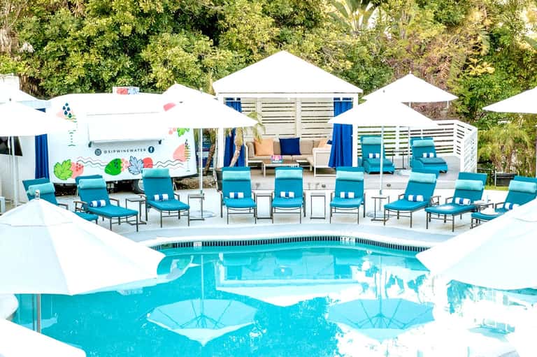 Turquoise resort pool with white umbrellas, lounge chairs, and modern beach cabanas
