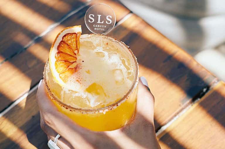 Signature cocktail with orange slice garnish and salt rim, labeled SLS Cancun Hotel