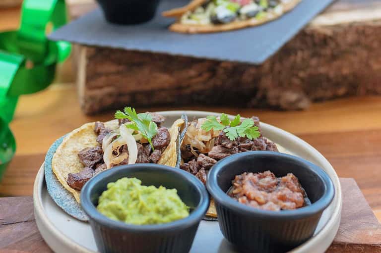 Plated beef tacos with guacamole and salsa on wooden surface