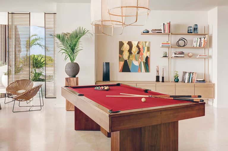 Modern game room with pool table, woven pendant light, wooden shelving, and tropical plant decor