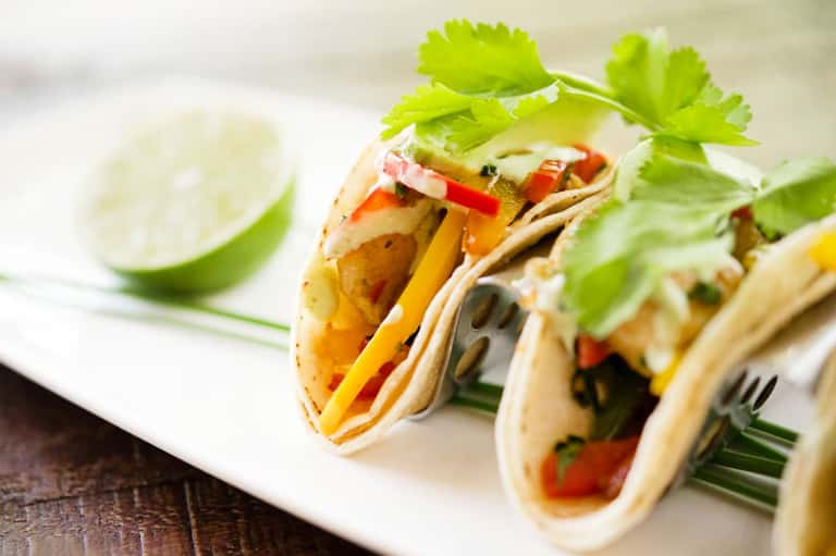 Colorful fish tacos with fresh cilantro garnish and lime wedge served on white plate