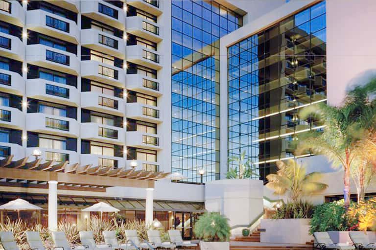 Modern hotel exterior with white buildings, glass atrium, pergolas, and illuminated landscaping at dusk