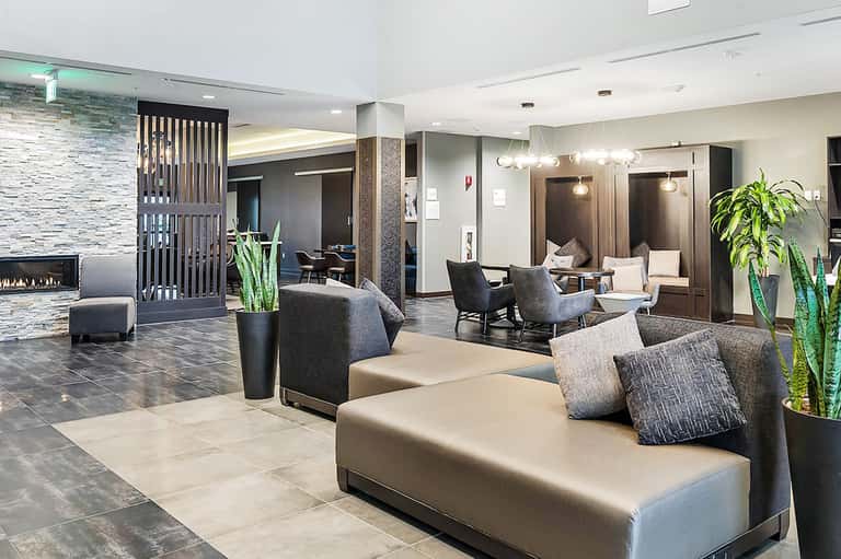 Contemporary hotel lobby featuring neutral tones, fireplace, modern furniture, and indoor plants