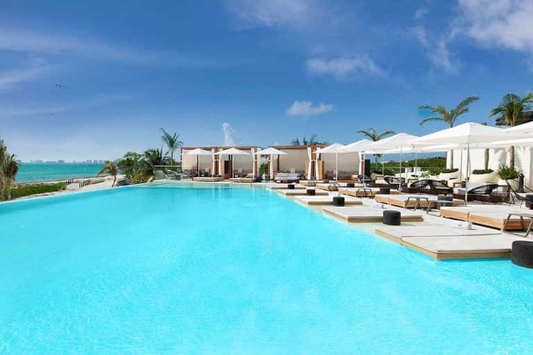 Expansive resort pool overlooking ocean with loungers, umbrellas, and coastal landscape at horizon