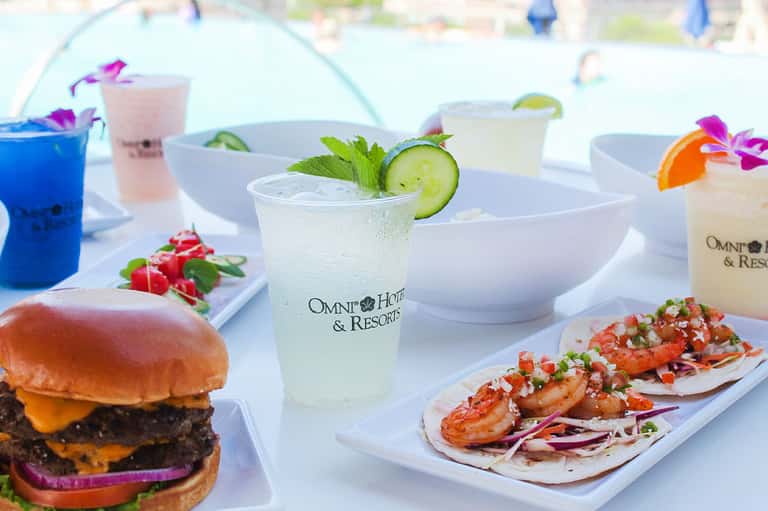 Gourmet food and beverage spread with cocktails, burger, and shrimp tacos at beachside venue