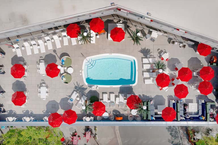 Aerial view of resort pool surrounded by red umbrellas and white lounge chairs