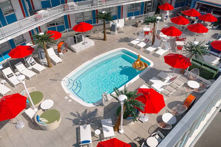 Aerial view of resort pool with red umbrellas and white lounge chairs on patio