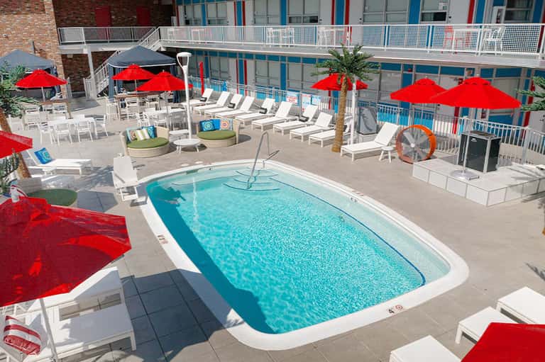 Resort pool with red umbrellas, white lounge chairs, and blue water under clear sky