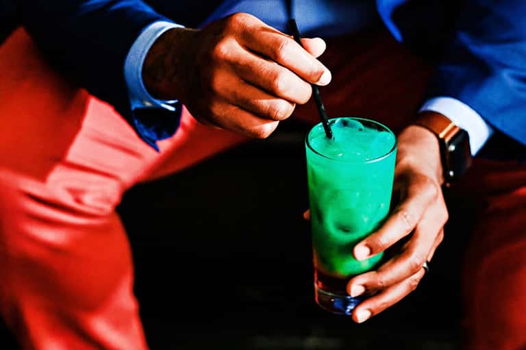 Person in formal attire holding bright green cocktail with straw