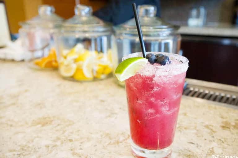 Pink cocktail with blueberries and lime garnish on stone counter with glass containers in background