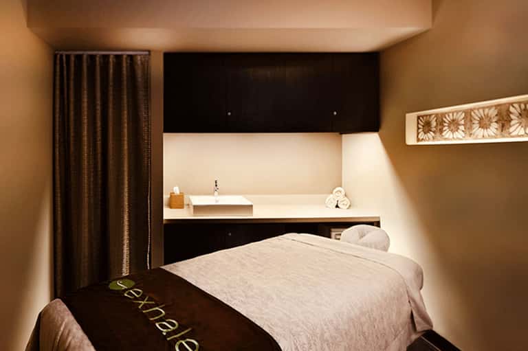 Spa massage room with modern design, dark headboard, bed, and sleek bathroom alcove