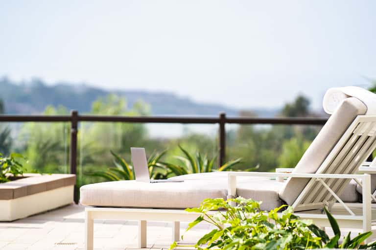 Modern lounge chairs and daybed on a sunny terrace with mountain views and flowering plants