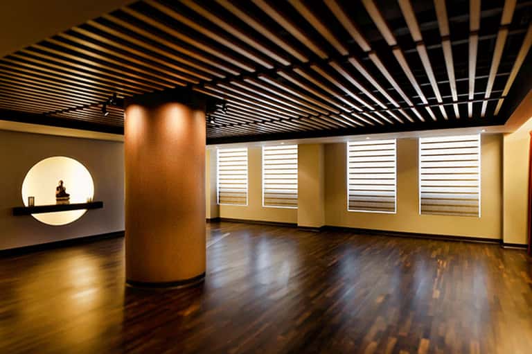 Modern interior space with black slatted ceiling, wooden flooring, and white horizontal shutter window treatments