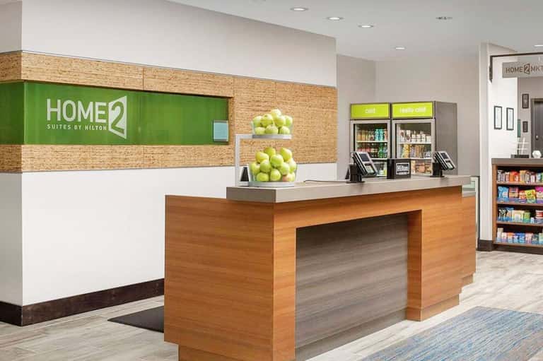 Home2 Suites hotel front desk with green signage, wooden reception counter, and merchandise displays