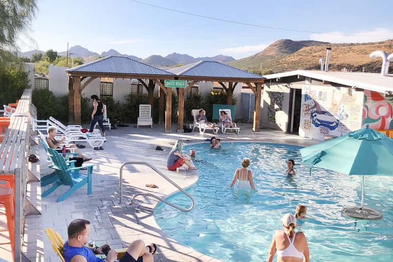 Casual pool area with families swimming, wooden pergola, and desert mountains
