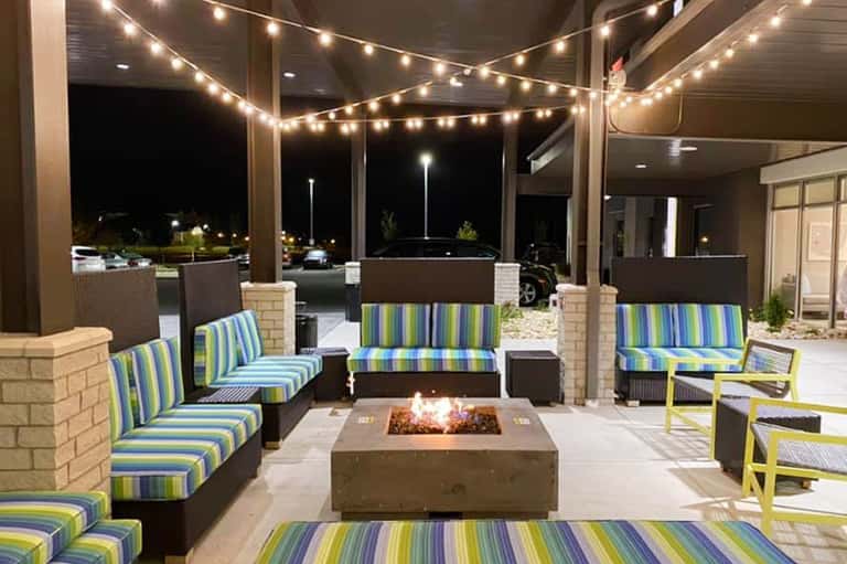 Outdoor patio at night with string lights, striped cushioned seating, and central fire pit